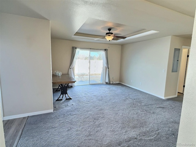 spare room with a raised ceiling, ceiling fan, electric panel, and dark carpet