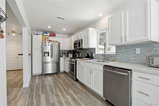 kitchen featuring white cabinets, light hardwood / wood-style flooring, sink, backsplash, and appliances with stainless steel finishes