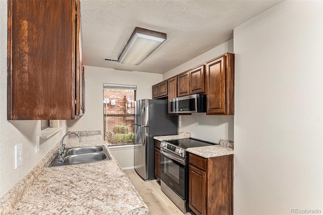 kitchen with a textured ceiling, appliances with stainless steel finishes, sink, and light hardwood / wood-style flooring