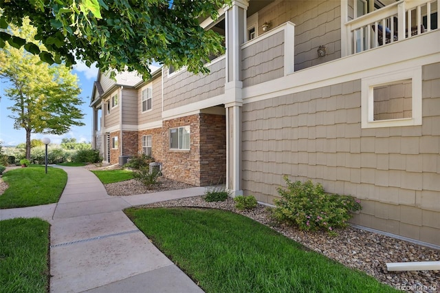 view of side of property with brick siding, central AC unit, and a lawn