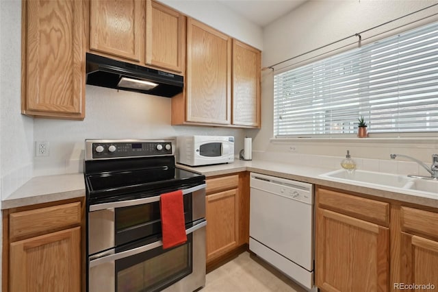 kitchen featuring white appliances, under cabinet range hood, a sink, and light countertops