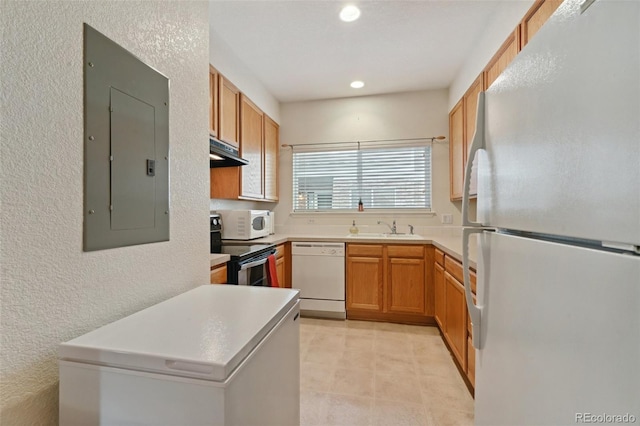 kitchen featuring white appliances, electric panel, under cabinet range hood, a textured wall, and light countertops