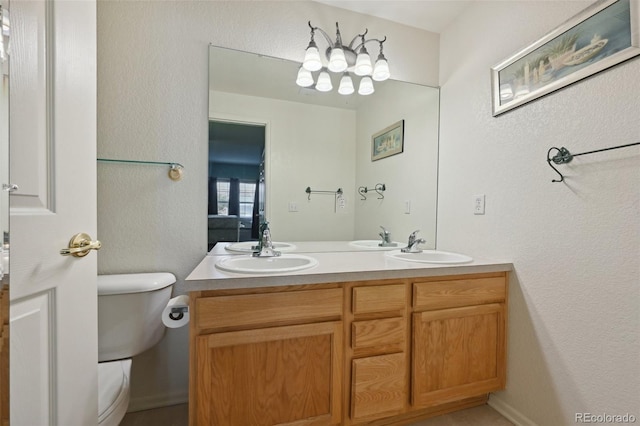 bathroom with double vanity, toilet, and a textured wall
