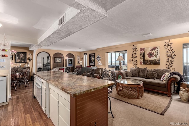 kitchen featuring a textured ceiling, dark wood-type flooring, white cabinets, and a kitchen breakfast bar