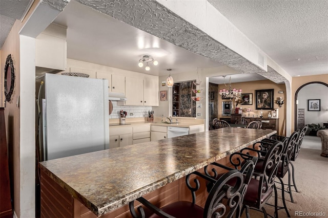 kitchen featuring a kitchen bar, tasteful backsplash, dishwasher, carpet flooring, and white cabinets