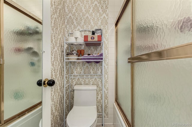 bathroom featuring toilet and bath / shower combo with glass door