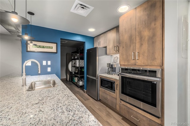 kitchen featuring decorative light fixtures, sink, light stone counters, and stainless steel appliances