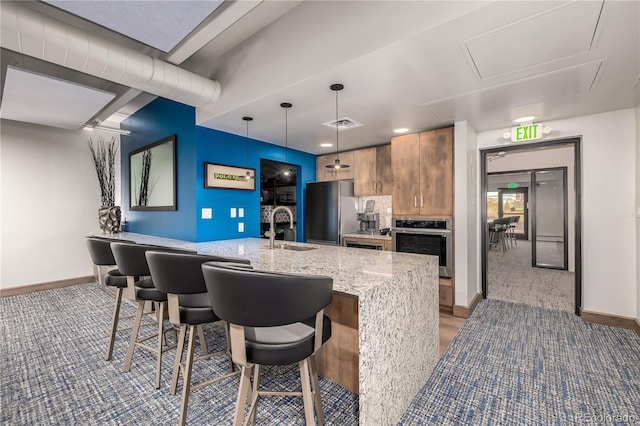 kitchen with pendant lighting, stainless steel appliances, sink, light stone counters, and a breakfast bar area