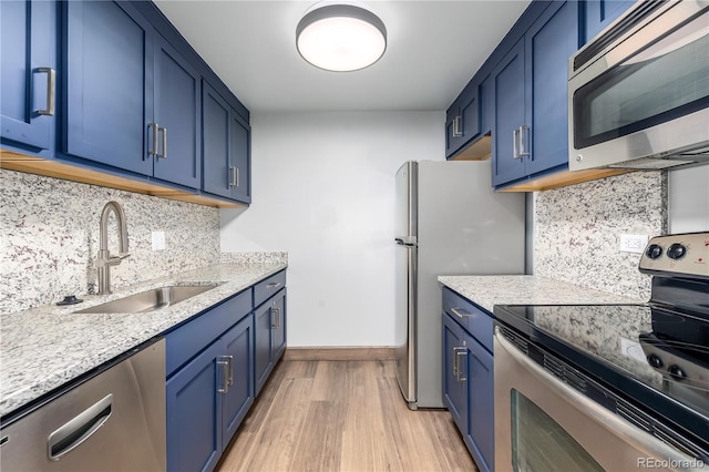 kitchen featuring appliances with stainless steel finishes, blue cabinetry, light stone countertops, light hardwood / wood-style flooring, and sink