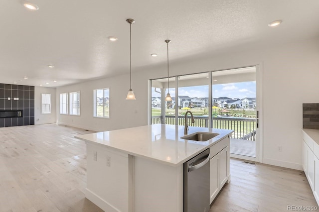 kitchen with pendant lighting, dishwasher, a center island with sink, sink, and white cabinetry