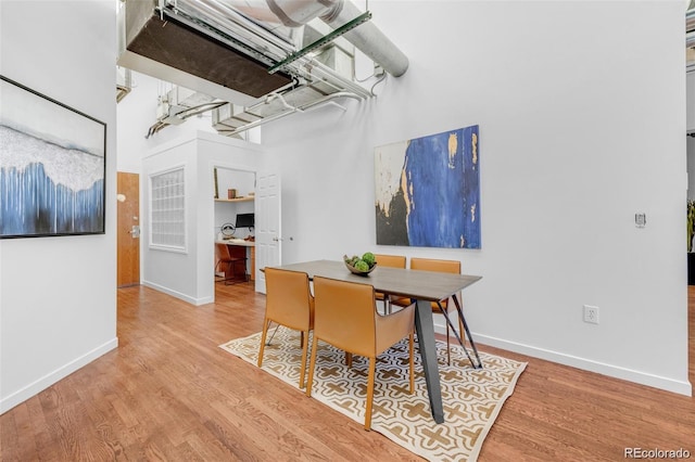 dining room with a towering ceiling, baseboards, and wood finished floors