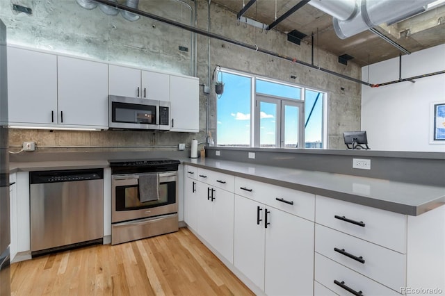 2020 Arapahoe St Unit 1250, Denver, CO 80205 - kitchen with a peninsula, stainless steel appliances, white cabinetry, dark countertops, and light wood-style floors