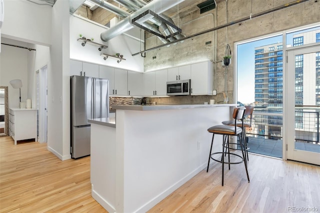 2020 Arapahoe St Unit 1250, Denver, CO 80205 - kitchen featuring a peninsula, light wood-style flooring, a kitchen bar, a high ceiling, and appliances with stainless steel finishes