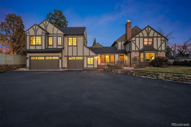 tudor house featuring aphalt driveway, a chimney, stucco siding, fence, and a garage