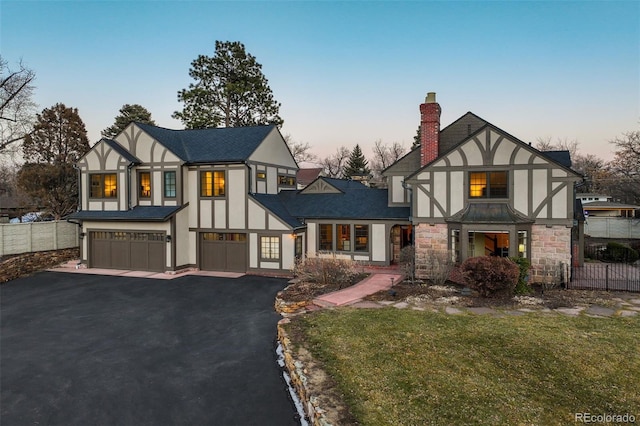 english style home with a garage, aphalt driveway, a chimney, and fence