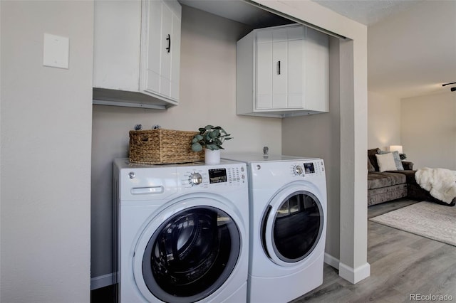 clothes washing area featuring washer and dryer, light hardwood / wood-style floors, and cabinets