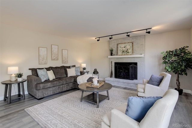 living room featuring wood-type flooring, track lighting, and a brick fireplace