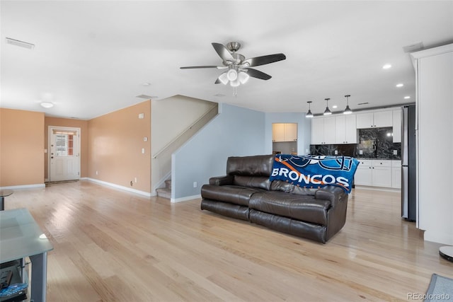 living area with stairs, light wood finished floors, a ceiling fan, baseboards, and recessed lighting