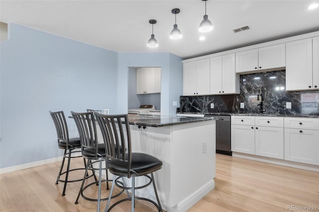 kitchen with light wood-type flooring, tasteful backsplash, dishwasher, and a center island