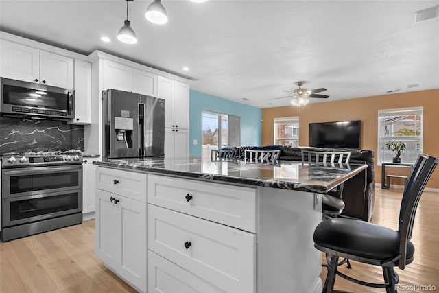 kitchen with stainless steel appliances, a kitchen breakfast bar, dark stone countertops, light wood finished floors, and ceiling fan