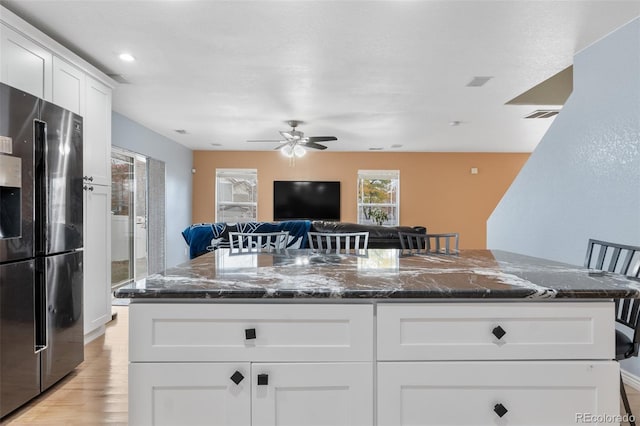 kitchen with light hardwood / wood-style floors, dark stone counters, a kitchen bar, white cabinets, and stainless steel fridge