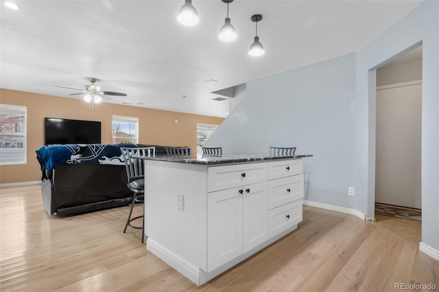 kitchen with a kitchen island, decorative light fixtures, white cabinets, a breakfast bar area, and light hardwood / wood-style flooring