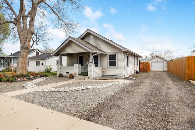 bungalow with covered porch, driveway, a detached garage, fence, and an outdoor structure