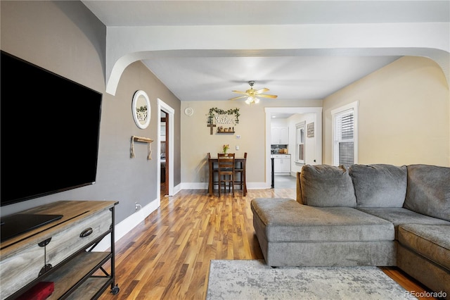 living area with baseboards, arched walkways, ceiling fan, and light wood-style flooring