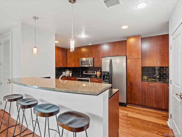 kitchen with appliances with stainless steel finishes, a kitchen breakfast bar, tasteful backsplash, decorative light fixtures, and light hardwood / wood-style flooring