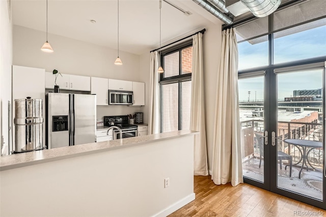 kitchen with white cabinets, light wood-style flooring, stainless steel appliances, light countertops, and pendant lighting