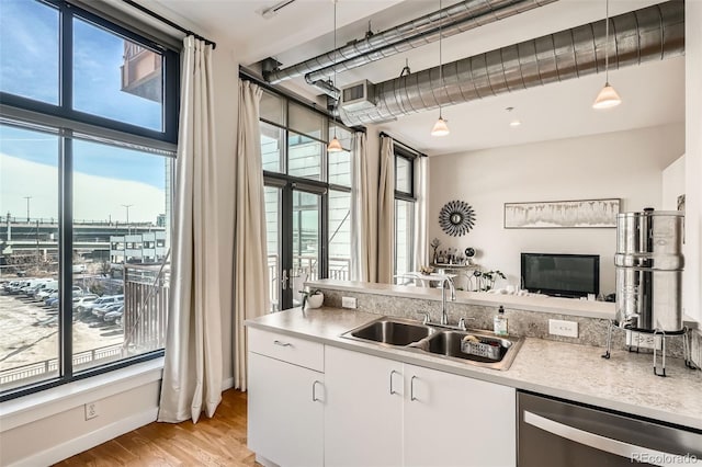 kitchen featuring white cabinets, dishwasher, light countertops, pendant lighting, and a sink