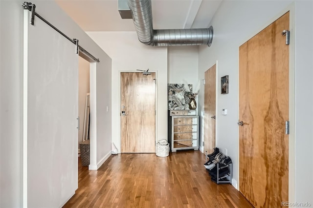 hallway featuring wood finished floors, baseboards, and a barn door