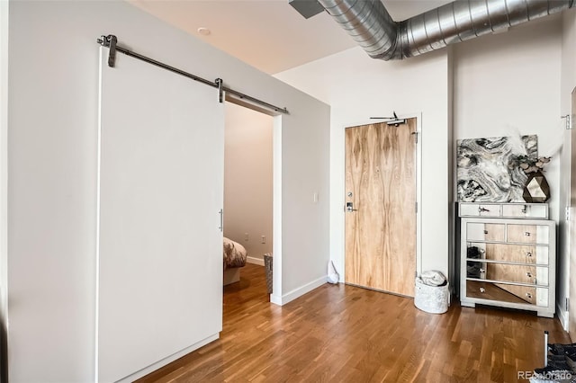 unfurnished bedroom with a barn door, baseboards, and wood finished floors