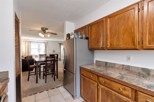 3407 S Ammons St Unit 20-2, Lakewood, CO 80227 - kitchen with freestanding refrigerator, ceiling fan, brown cabinets, light colored carpet, and a textured ceiling