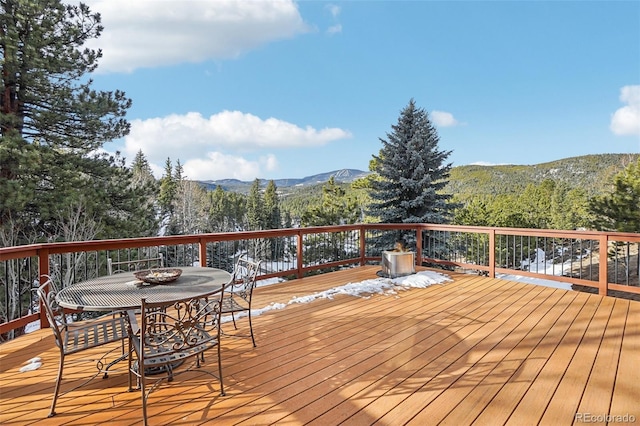 wooden terrace with outdoor dining area, a mountain view, and a view of trees