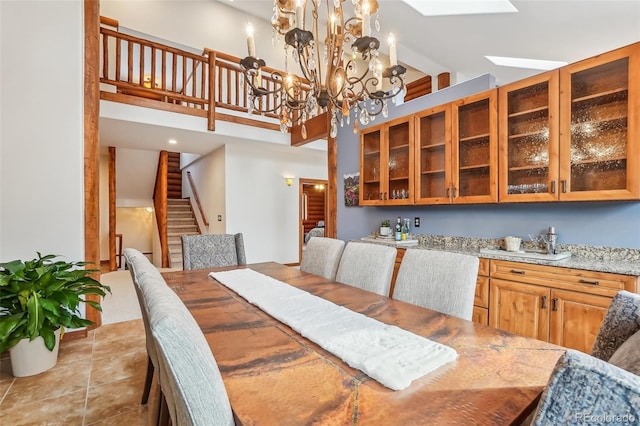 dining space featuring light tile patterned floors, a high ceiling, a skylight, stairway, and an inviting chandelier