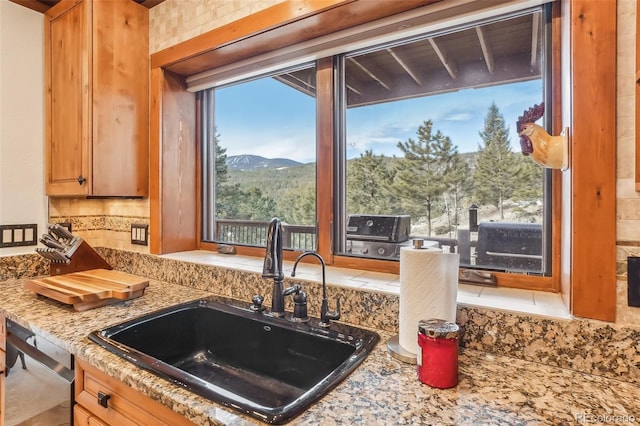 kitchen featuring dishwashing machine, light stone counters, a mountain view, a sink, and tasteful backsplash