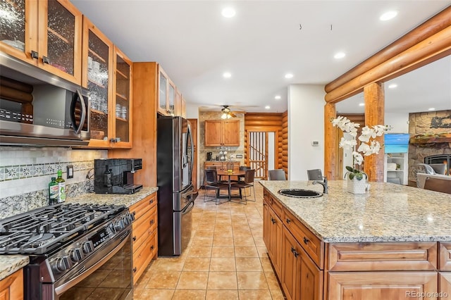 kitchen featuring light stone counters, tasteful backsplash, rustic walls, appliances with stainless steel finishes, and a sink