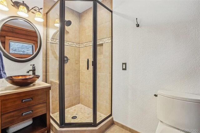 bathroom featuring a textured wall, toilet, a shower stall, and vanity