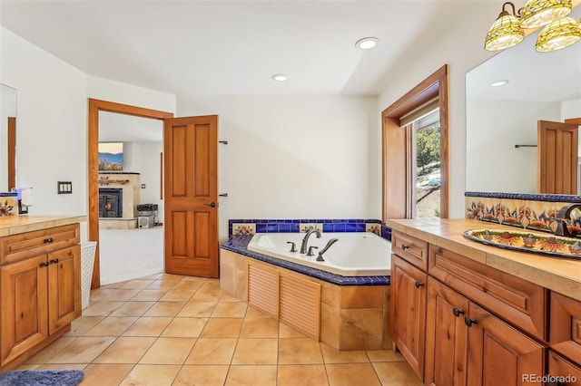 bathroom with recessed lighting, vanity, a bath, tile patterned floors, and a tiled fireplace