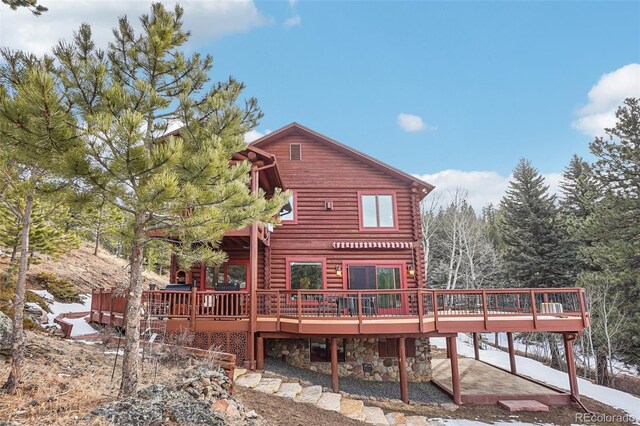 back of house featuring stone siding, log exterior, and a deck