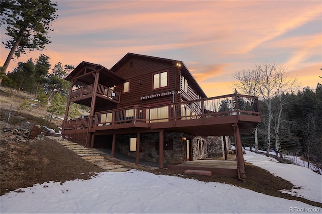 snow covered rear of property featuring a deck and stone siding