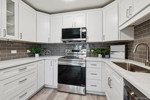 kitchen featuring sink, light stone counters, light hardwood / wood-style floors, stainless steel appliances, and white cabinets