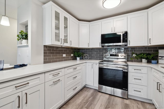 kitchen featuring light wood-type flooring, white cabinets, stainless steel appliances, and hanging light fixtures