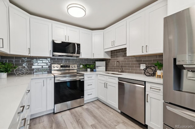 kitchen with sink, backsplash, light hardwood / wood-style floors, stainless steel appliances, and white cabinets