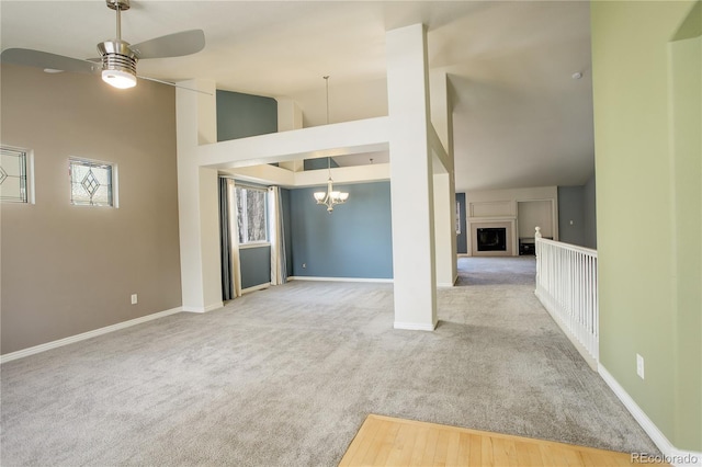 carpeted empty room featuring ceiling fan with notable chandelier and high vaulted ceiling