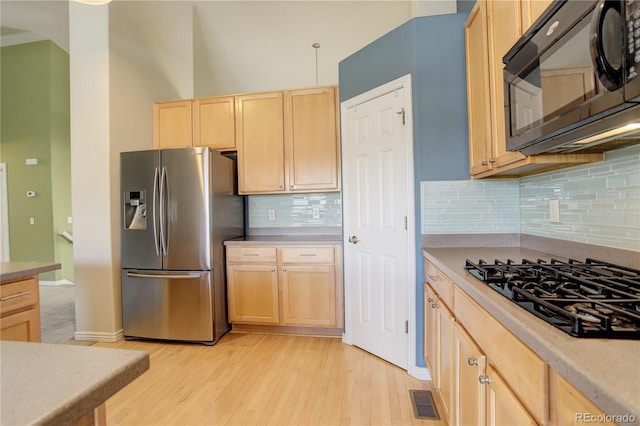 kitchen with decorative backsplash, light brown cabinetry, light hardwood / wood-style flooring, and black appliances