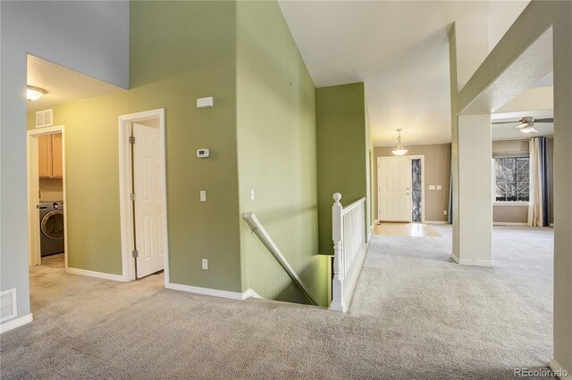 hallway featuring a towering ceiling, washer / dryer, and light carpet