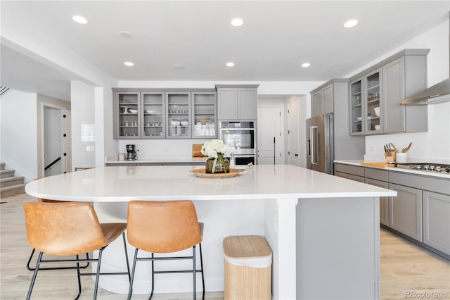 kitchen featuring a kitchen breakfast bar, stainless steel appliances, wall chimney exhaust hood, and a spacious island