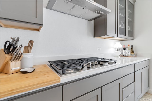 kitchen with stainless steel gas stovetop, wall chimney exhaust hood, and gray cabinets